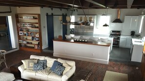 A spacious living area with a large sofa, a coffee table, and a bookshelf. A kitchen with modern appliances is visible in the background.