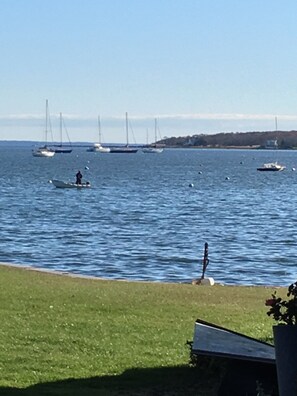 A coastal scene with boats on the water, a grassy area, and a distant shoreline. - Mattapoisett Village Waterfront (Mattapoisett)