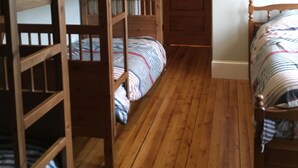A room with bunk beds, wooden flooring, a door, and framed pictures on the wall.