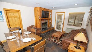 A cozy living room with a fireplace, wooden furniture, and a dining area with a table set for four.