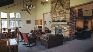 A spacious living area with a stone fireplace, wooden furniture, and large windows allowing natural light.