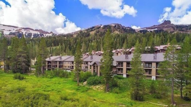A hotel with multiple buildings surrounded by lush greenery and mountains in the background.