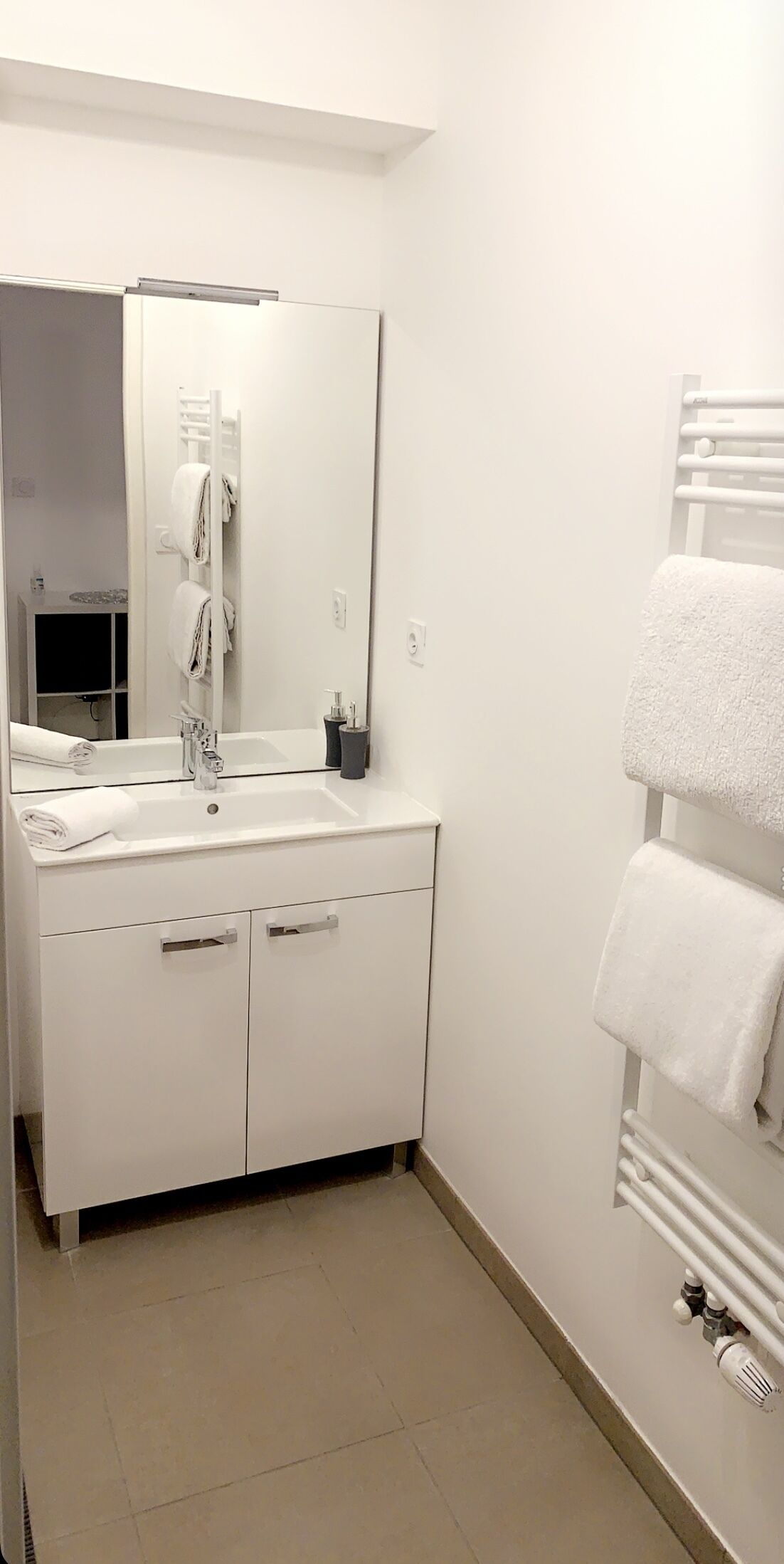 A modern bathroom with a white sink, mirror, and towel rack.