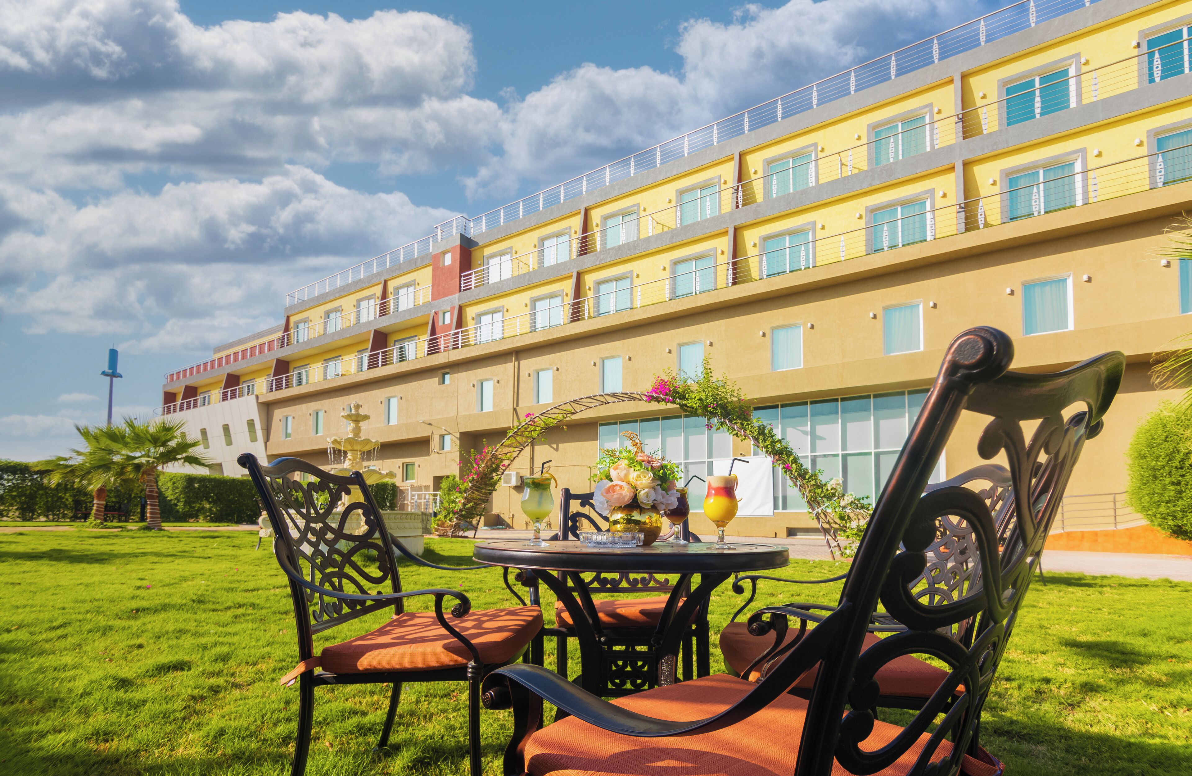 A hotel with a yellow facade, multiple balconies, and a garden area with outdoor seating.