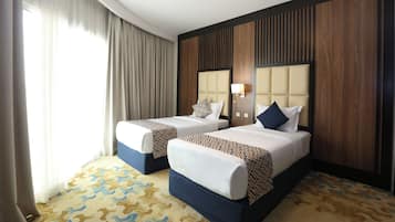 Ein Hotelzimmer mit zwei Betten, einem gemusterten Teppich und einem großen Fenster mit Vorhängen.