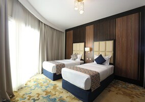 Habitación de hotel con dos camas, alfombra estampada y un ventanal con cortinas.