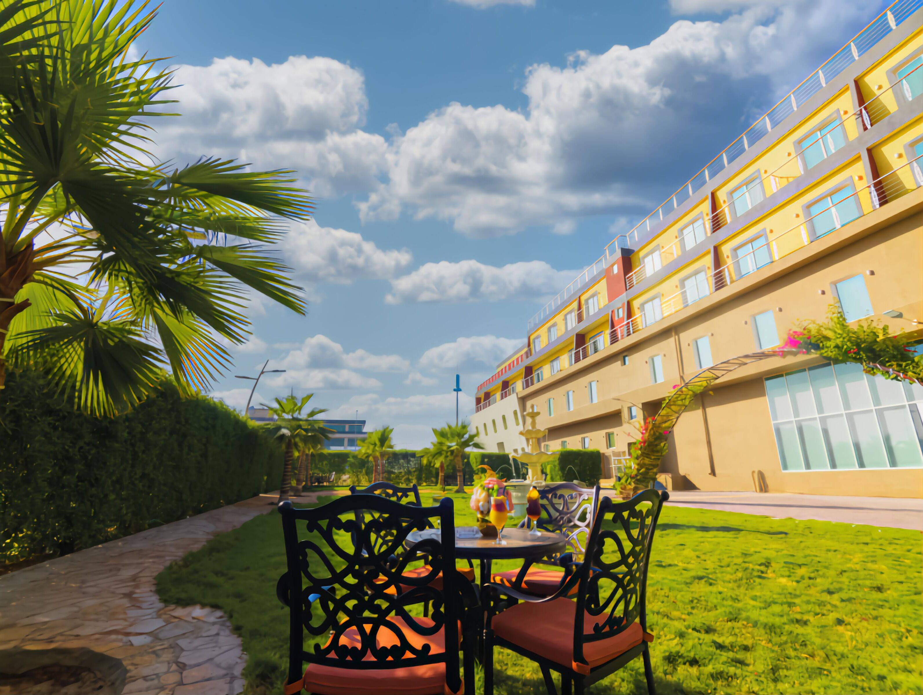 A courtyard with a table and chairs, surrounded by greenery and a building with balconies.