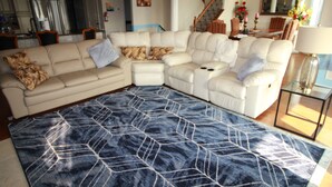 Un salon avec un canapé d’angle, un tapis à motifs et un escalier.