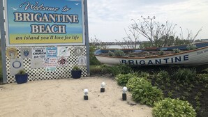 Un panneau de signalisation sur la plage accueillant les visiteurs de Brigantine Beach, avec un bateau portant le nom « BRIGANTINE » et divers logos représentant la communauté et les églises.