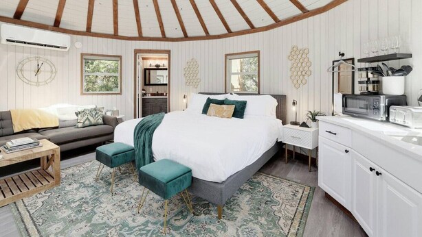 A bedroom with a bed, bedside tables, a sofa, a rug, and a kitchen area with appliances.