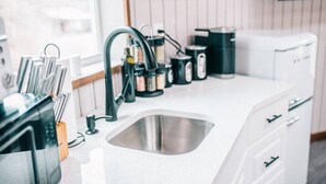 A modern kitchen with a stainless steel sink, a black faucet, and a white countertop. There are cabinets and a microwave on the counter.