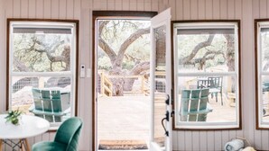 A room with a large window, a dining table with chairs, and a view of an outdoor deck.