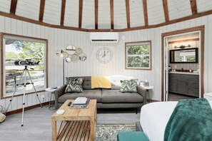 A cozy room with a sofa, a coffee table, and a bed. There's a telescope on a tripod by a window, and a mirror on the wall. - Breathtaking Treehouse Yurt! King Bed and Spa! (Dripping Springs)