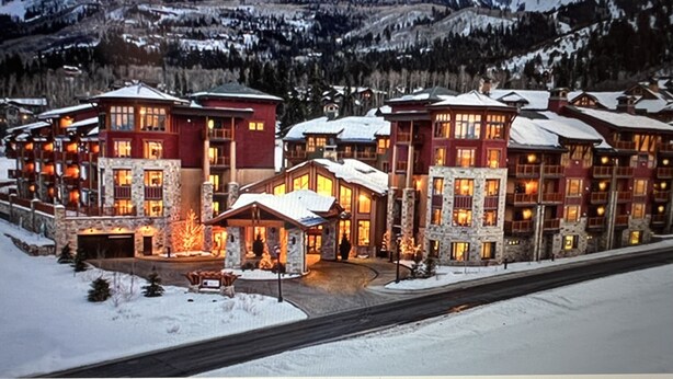 A large lodge with multiple buildings, a central fireplace area, and a view of snow-covered mountains in the background. - Beautiful Ski in and Ski out Lodge (Park City)