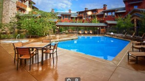 A swimming pool with lounge chairs and a table, surrounded by buildings with balconies and a clear sky. - Beautiful Ski in and Ski out Lodge (Park City)