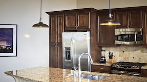 A kitchen with granite countertops, stainless steel appliances, dark wooden cabinets, and pendant lighting. - Beautiful Ski in and Ski out Lodge (Park City)