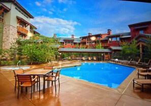 A swimming pool with lounge chairs and a table, surrounded by buildings with balconies and a clear sky. - Beautiful Ski in and Ski out Lodge (Park City)