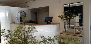 Un comptoir d’accueil avec une horloge, un ordinateur et un vase rempli de fleurs.