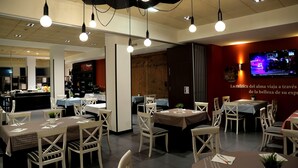 Un restaurante con mesas, sillas, una barra y un televisor instalado en la pared.