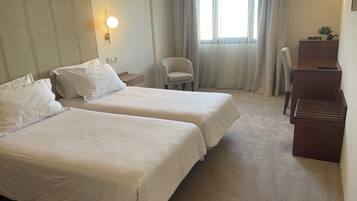 A hotel room with two beds, a desk, a chair, and a window with curtains.