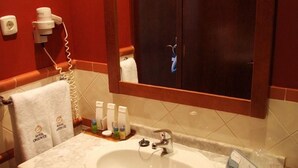 Un baño con lavamanos de mármol, un perchero con toalla, un espejo, un dispensador de jabón y un secador de manos.