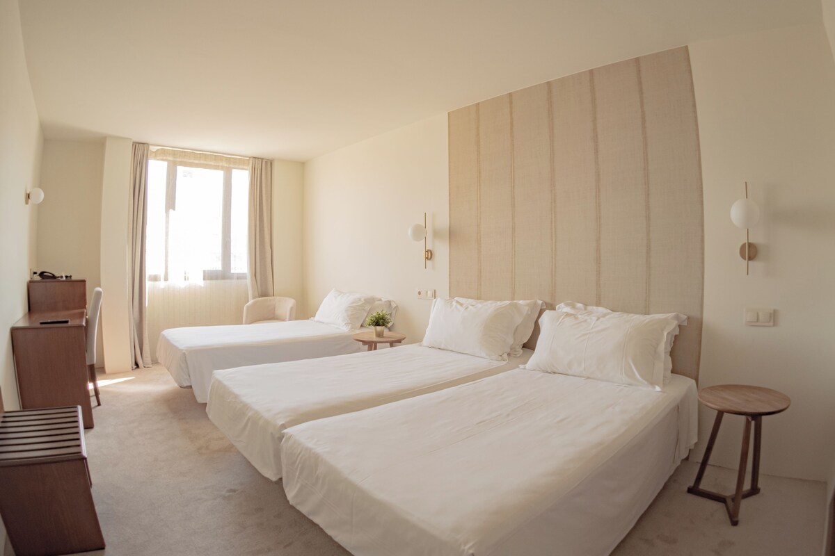 Habitación de hotel con dos camas, un escritorio, una silla, una mesita y una ventana con cortinas.