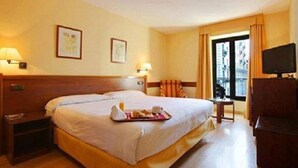 Una habitación de hotel con una cama grande, mesitas de noche, un televisor y una ventana con cortinas.