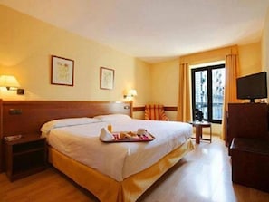 Ein Hotelzimmer mit einem großen Bett, Nachttischen, einem Fernseher und einem Fenster mit Vorhängen.