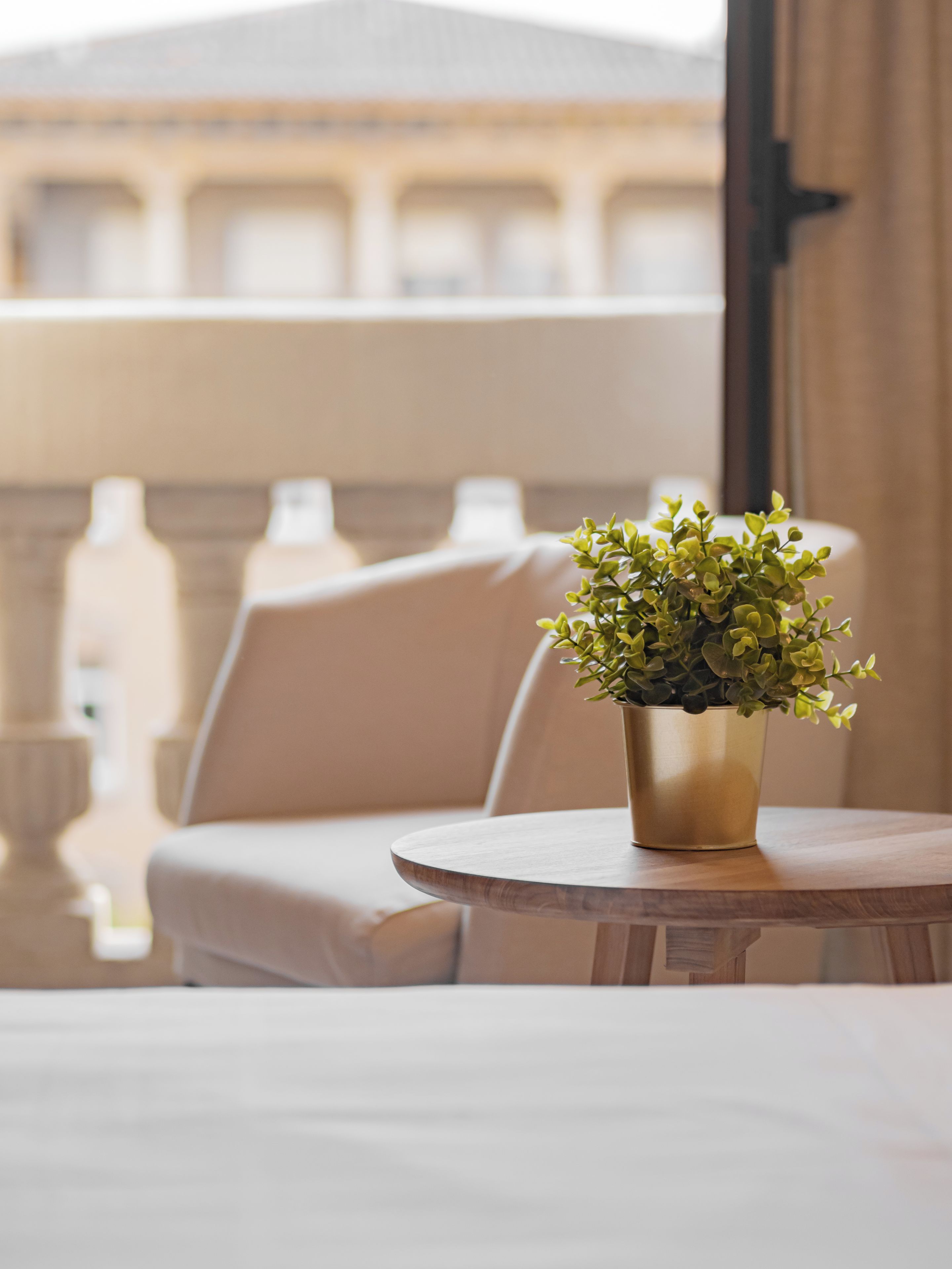 A round table with a potted plant, a beige sofa, and a view of a building with balconies.