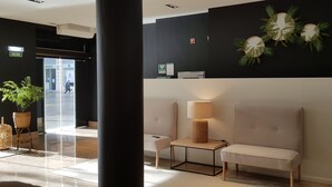 Vestíbulo con mostrador de recepción, dos zonas de estar, planta en la pared y una puerta con la señalización 'SALIDA'.