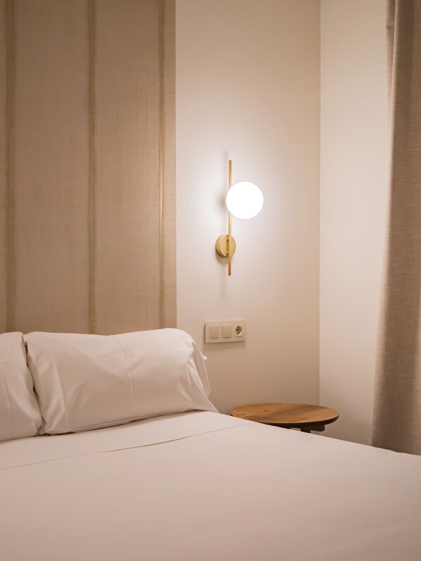 Une chambre d’hôtel équipée d’un lit, d’une table de chevet, d’une lampe fixée au mur et d’une prise de courant.