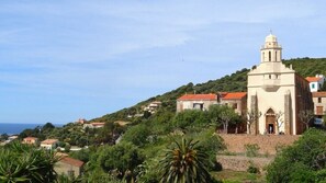 A coastal town with a prominent church featuring a bell tower, surrounded by lush greenery and residential buildings. - House (Cargèse)