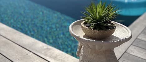 Uma pequena planta em vaso sobre um pedestal branco, perto de uma piscina com vista clara para o oceano.