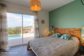 A bedroom with a large bed, a view of the outdoors, and a wooden headboard. - House (Cargèse)