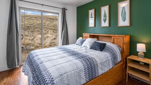 Ein Schlafzimmer mit einem großen Bett, einem Holzkopfende, einem Nachttisch mit Lampe und Blick auf eine grüne Landschaft durch ein Fenster.