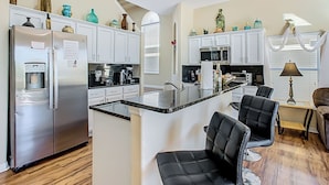 A modern kitchen with white cabinets, stainless steel appliances, and a central island with chairs. - Triton Pool/Spa  Home Near Disney With Spa & Resort Perks (Clermont)