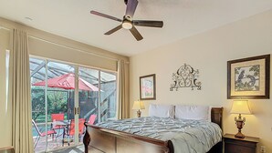 A bedroom with a large bed, a ceiling fan, a window with curtains, and a view of an outdoor patio. - Triton Pool/Spa  Home Near Disney With Spa & Resort Perks (Clermont)