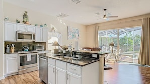 A modern kitchen with white cabinetry, stainless steel appliances, and a large island. - Triton Pool/Spa  Home Near Disney With Spa & Resort Perks (Clermont)
