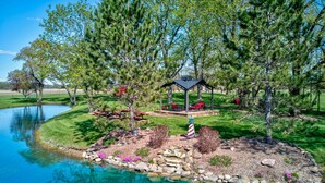 A serene lakeside setting with a gazebo, clear water, and surrounding greenery. - Peaceful 2BR Farm Stay - 10 Min To Grand Park (Sheridan)