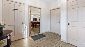 A hallway with three white doors, a wooden floor, and a small table with a vase of flowers. - Peaceful 2BR Farm Stay - 10 Min To Grand Park (Sheridan)
