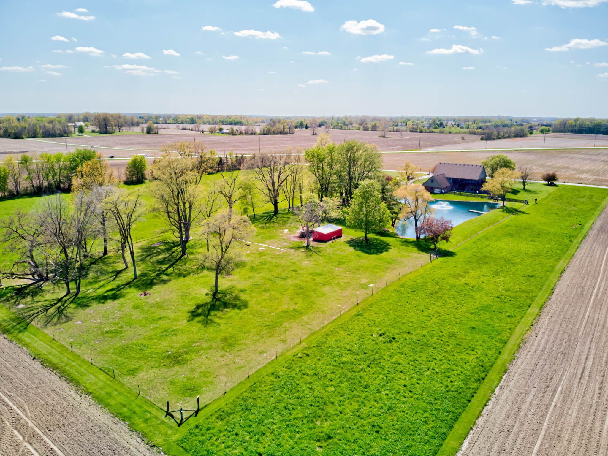 An aerial view of a rural property with a swimming pool, a red barn, and open fields.
