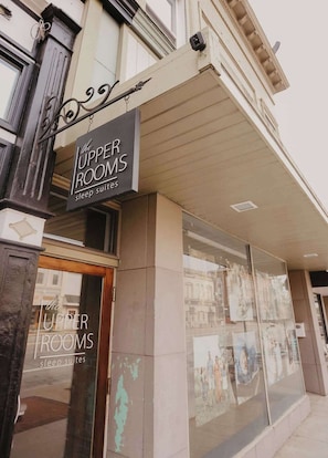 The exterior of 'The Upper Rooms' sleep suites with a large glass window and a metal sign. - Beautiful Downtown Loft - East Suite (Clare)