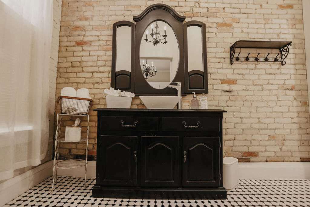 A bathroom with a black vanity, a mirror, a chandelier, and a brick wall.