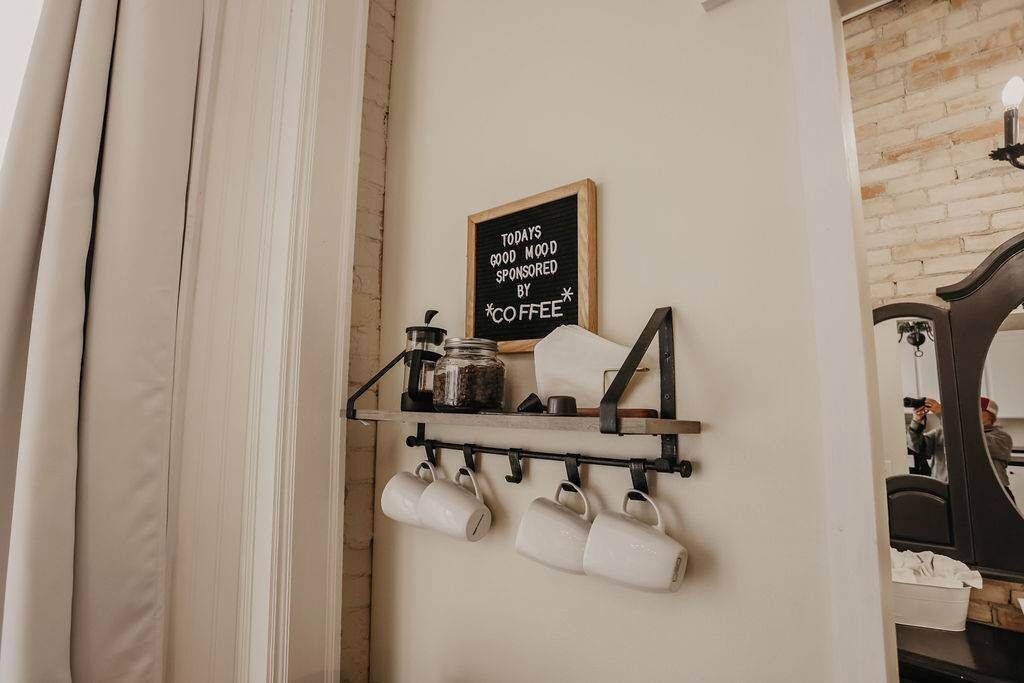 A kitchen area with a chalkboard sign, a shelf with mugs, and a coffee maker.