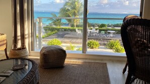 Une pièce dotée d’une grande porte-fenêtre coulissante donnant sur un balcon avec vue sur l’océan et les palmiers.