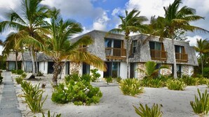 Un hôtel situé en bord de mer, doté de nombreuses chambres, de palmiers et d’une promenade bordée de sable.