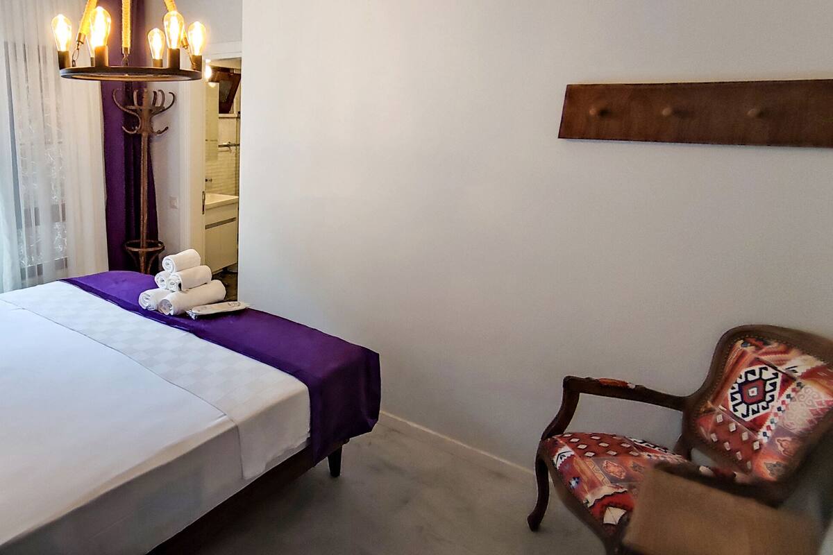 A hotel room with a bed, a chair, a lamp, and a chandelier.