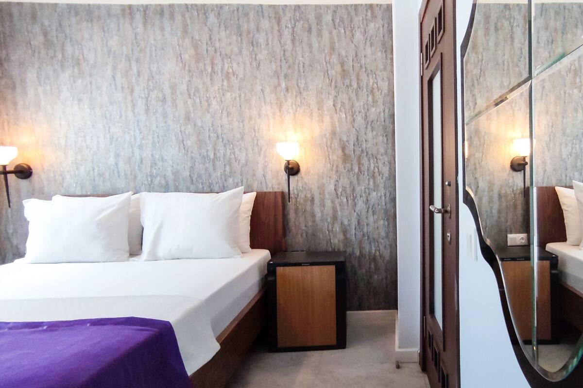 A hotel room with two beds, a small bedside table, a nightstand, and a mirror.
