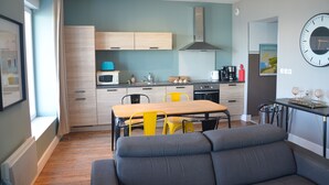 A modern kitchen with wooden cabinets, a dining table with yellow chairs, and a grey sofa in the foreground.