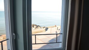 A view from a window overlooking a calm sea and a rocky shoreline with a paved walkway.